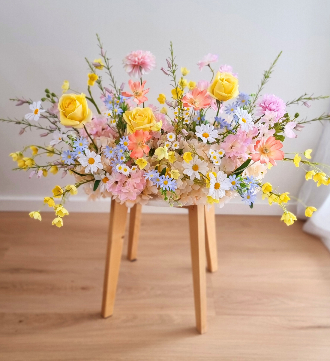 Pastel wildflower silk arrangement in yellow, pink, coral, and blue on a wooden stool