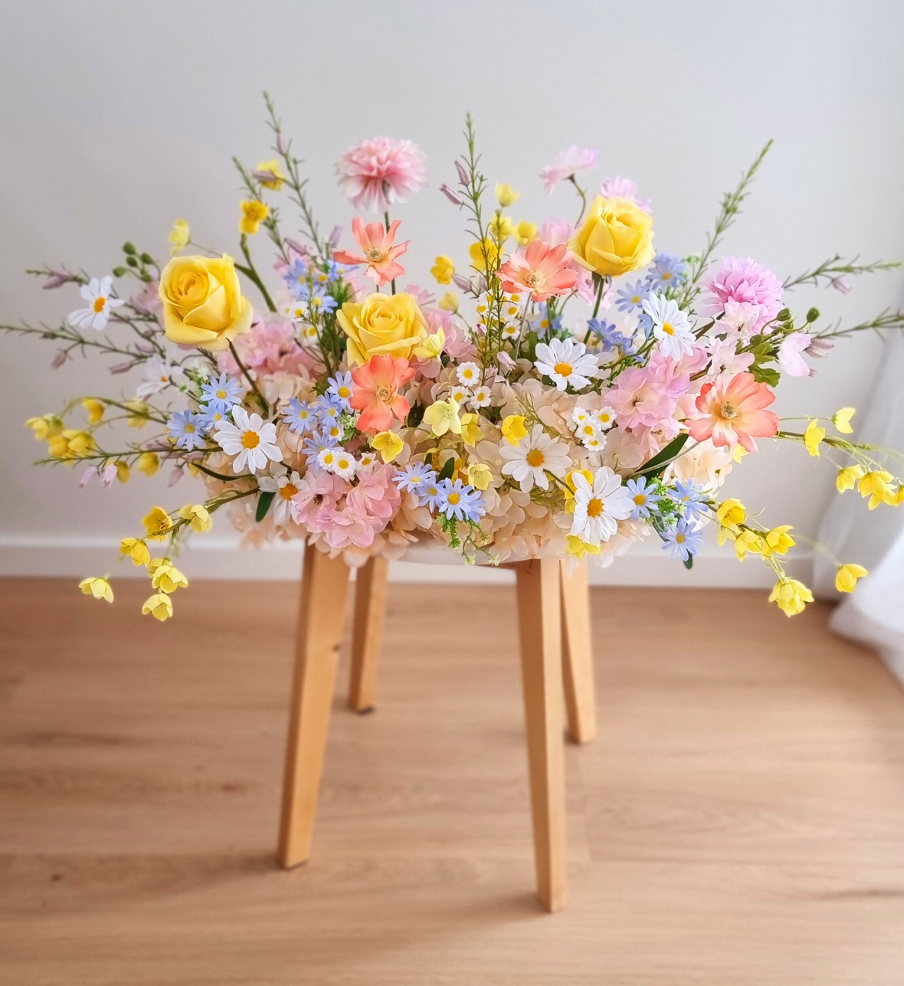 Pastel wildflower silk arrangement in yellow, pink, coral, and blue on a wooden stool