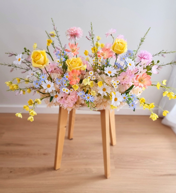 Pastel wildflower silk arrangement in yellow, pink, coral, and blue on a wooden stool