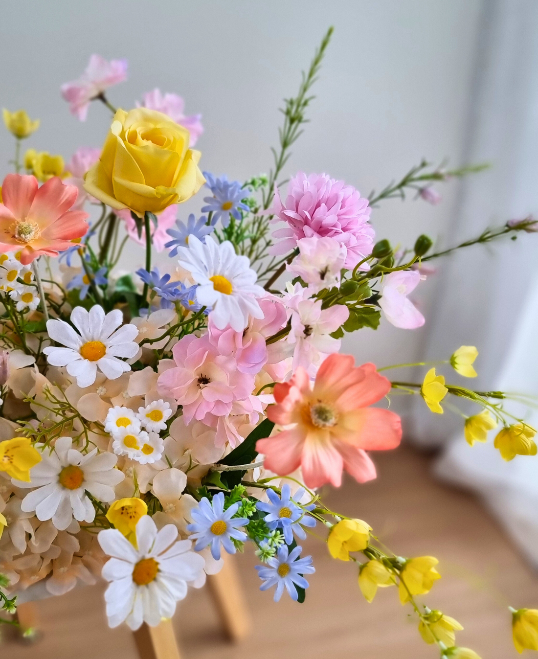 Pastel wildflower silk arrangement in yellow, pink, coral, and blue on a wooden stool